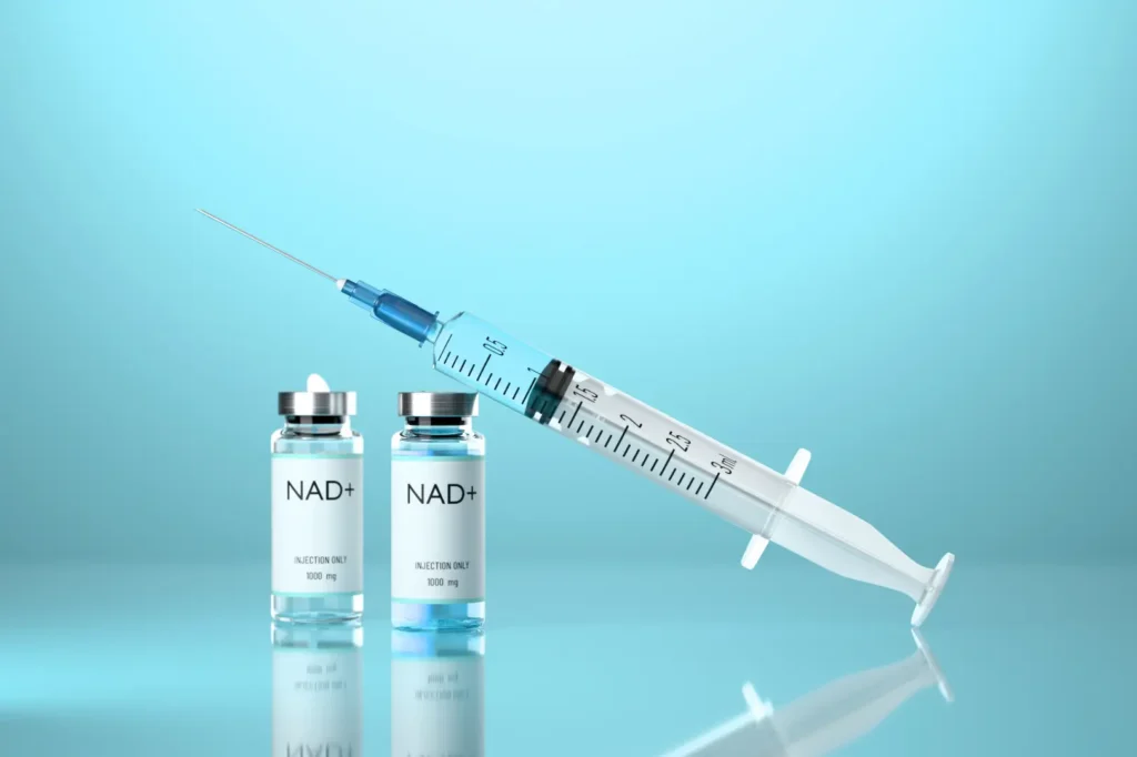 Two labeled NAD+ vials beside a syringe on a blue surface.