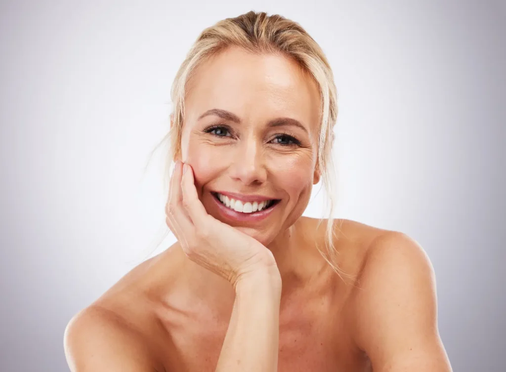 Smiling woman resting her face on one hand against a light background.