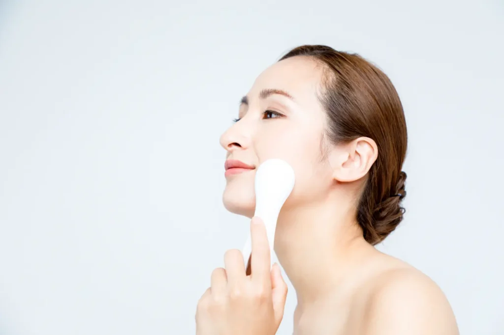 Woman using a handheld facial massage tool along her jawline.
