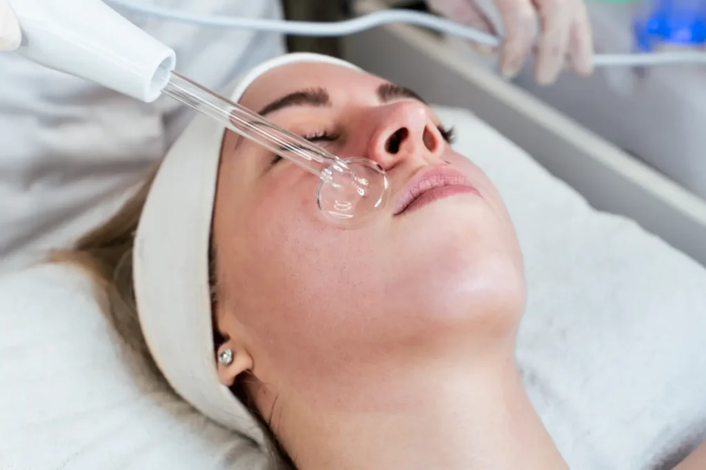 Woman lies on a treatment bed while a glass-tipped device is positioned against her cheek.